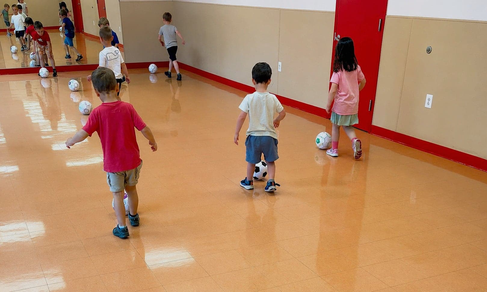 Cubs dribbling soccer balls across the floor during a Soccer Cubs class